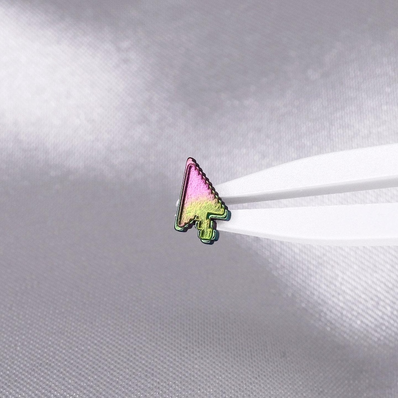 May include: A small, iridescent computer mouse cursor icon pin featuring a gradient of vibrant pink and lime green colors. The metallic cursor shape is held by white plastic tweezers, showcasing its distinct pixelated edge design and reflective finish.