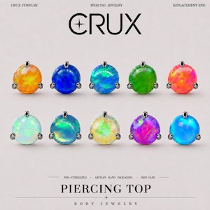 Può includere: Dieci terminali per piercing a cabochon rotondo con montature in metallo scuro, disposti su due file. Ognuno presenta un opale sintetico iridescente in colori vivaci tra cui arancione, blu, verde, rosa, bianco e viola. Testo: CRUX JEWELRY PIERCING TOP.