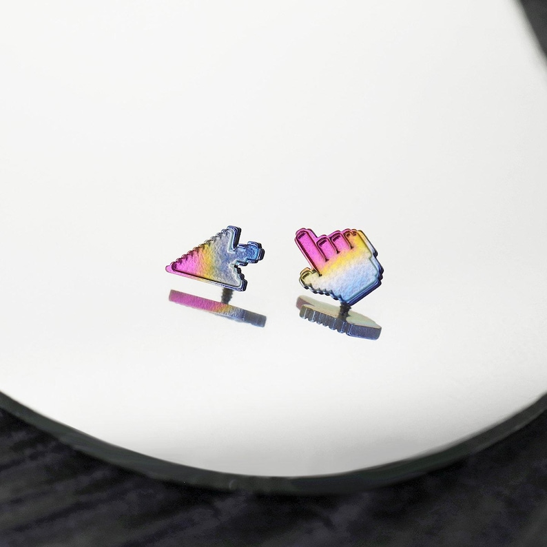 May include: A pair of stud earrings shaped like computer mouse cursors, one as a standard arrow and the other as a pointing hand. The earrings feature a metallic rainbow gradient finish that transitions between shades of blue, purple, pink, and yellow.