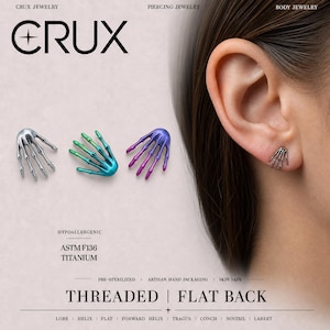 May include: Three skeleton hand stud earrings in silver, teal-green, and purple-blue gradient colours. One silver skeleton hand earring is shown inserted into an earlobe. The text includes CRUX JEWELRY, HYPOALLERGENIC, ASTM F136 TITANIUM, and THREADED FLAT BACK.