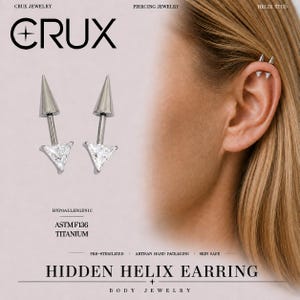 Puede incluir: Dos pendientes de hélix plateados con una punta cónica y una base de piedra preciosa transparente de corte triangular. El texto CRUX, HYPOALLERGENIC, ASTM F136 TITANIUM y HIDDEN HELIX EARRING es visible. Se muestran puestos en un piercing.
