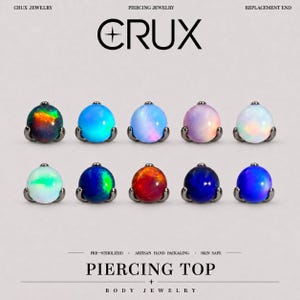 May include: Ten round cabochon piercing tops arranged in two rows. Each piece features a colourful, iridescent stone set in a dark metal prong setting. The text CRUX JEWELRY PIERCING JEWELRY REPLACEMENT END and PIERCING TOP BODY JEWELRY is visible.