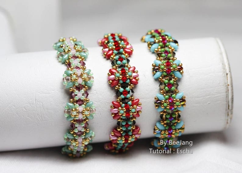 May include: Three beaded bracelets with intricate floral patterns. The bracelets feature a variety of colors, including red, pink, green, and gold. The bracelets are displayed on a white cylindrical surface.