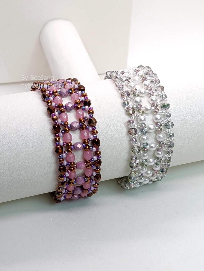 Two wide, handcrafted beaded cuff bracelets are displayed on a white stand, showcasing an intricate Right Angle Weave lattice design. Both pieces are meticulously woven with faceted bicone crystals, smooth round pearls, and delicate seed beads.

    Left: A warm palette of pink and lavender beads accented by dark metallic bronze rounds.
    Right: A monochromatic, elegant look featuring translucent clear crystals and lustrous white pearls.