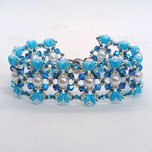 May include: A beaded bracelet with a floral pattern. The bracelet is mainly light blue, with darker blue and silver accents. White pearl beads are incorporated into the design. The bracelet is approximately 18 cm in length.