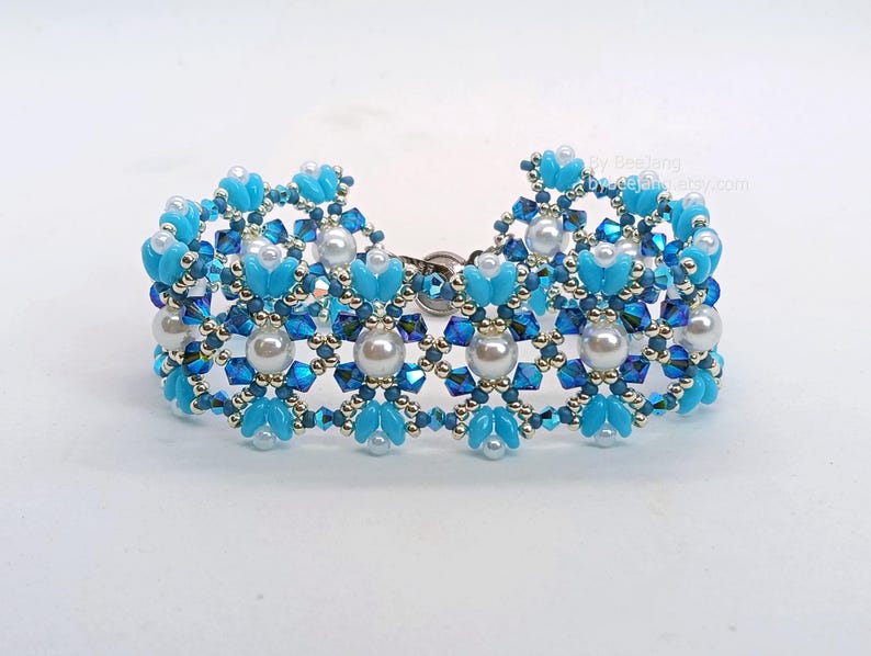 May include: A beaded bracelet with a floral pattern. The bracelet is mainly light blue, with darker blue and silver accents. White pearl beads are incorporated into the design. The bracelet is approximately 18 cm in length.