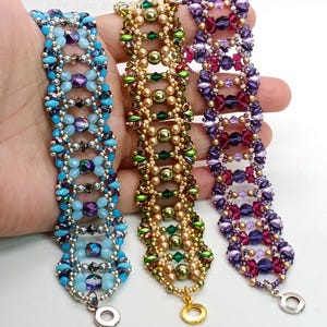 Puede incluir: Tres pulseras de cuentas en tonos azules, dorados y morados. La pulsera azul presenta cuentas azules claras y oscuras con detalles plateados. La pulsera dorada tiene cuentas doradas y verdes. La pulsera morada tiene cuentas moradas y rosas. Cada pulsera tiene un cierre met&aacute;lico.