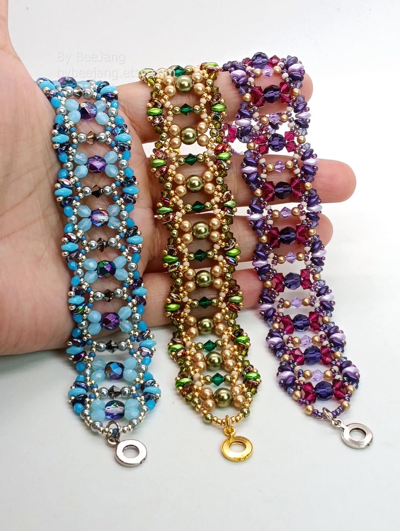 Puede incluir: Tres pulseras de cuentas en tonos azules, dorados y morados. La pulsera azul presenta cuentas azules claras y oscuras con detalles plateados. La pulsera dorada tiene cuentas doradas y verdes. La pulsera morada tiene cuentas moradas y rosas. Cada pulsera tiene un cierre met&aacute;lico.