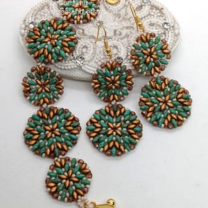 Könnte beinhalten: Handgefertigter Schmuck, bestehend aus Ohrringen und einem Armband. Die Stücke weisen ein Blumenmuster mit türkis-, bronze- und weißen Perlen auf. Die Ohrringe haben goldfarbene Haken. Der Schmuck wird auf einer weißen, strukturierten Oberfläche präsentiert.