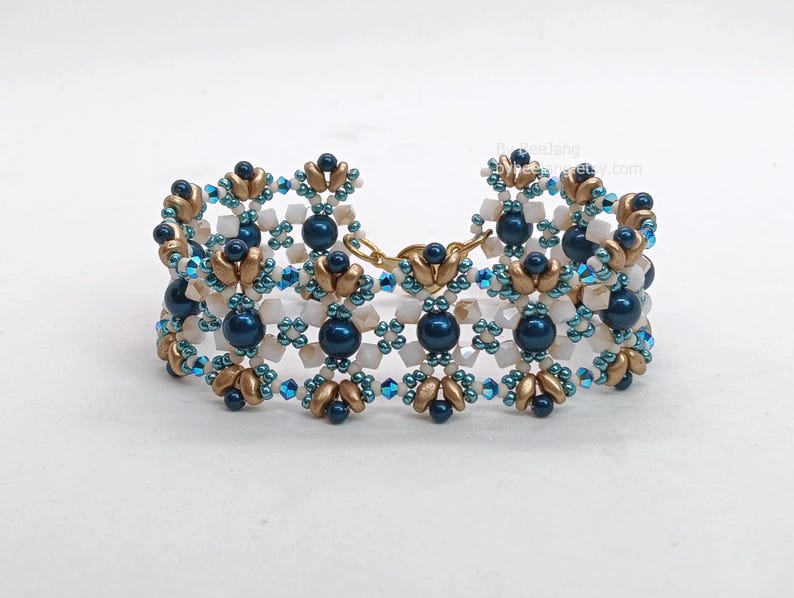 May include: A beaded bracelet with a repeating pattern of navy blue, gold, and white beads. The bracelet has a gold-coloured clasp and is designed with a floral motif. The beads are arranged in a symmetrical design.