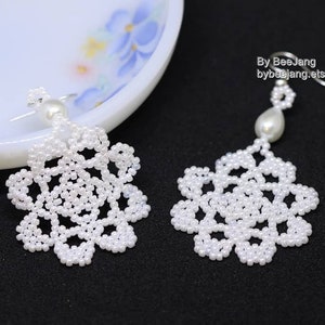May include: A pair of white beaded earrings with a pearl drop. The earrings are made of small white beads that are strung together to create a delicate and intricate design. The earrings are perfect for a special occasion or everyday wear.
