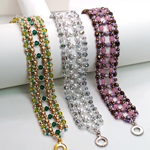 Three wide, handcrafted cuff bracelets are displayed, showcasing an intricate
Right Angle Weave lattice design. Each piece is meticulously woven with faceted bicone crystals, smooth round pearls, and delicate seed beads, secured with a metallic toggle clasp. The left is green emerald and olive crystals with bronze pearls. The middle is translucent clear crystals with white pearls and silver accents. The right is deep purple and lavender crystals with copper-colored beads.