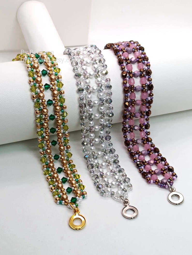 Three wide, handcrafted cuff bracelets are displayed, showcasing an intricate
Right Angle Weave lattice design. Each piece is meticulously woven with faceted bicone crystals, smooth round pearls, and delicate seed beads, secured with a metallic toggle clasp. The left is green emerald and olive crystals with bronze pearls. The middle is translucent clear crystals with white pearls and silver accents. The right is deep purple and lavender crystals with copper-colored beads.