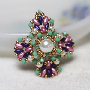 May include: A beaded flower brooch with a pearl centre. The flower is made with gold, pink, purple, and green beads.