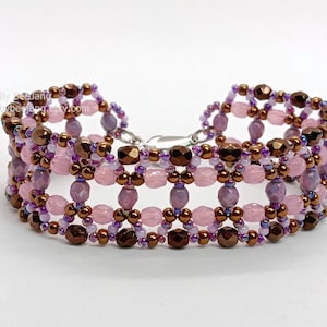 A wide, handcrafted beaded cuff bracelet featuring an intricate, open-lattice
Right Angle Weave design. The piece is constructed with faceted pink and lavender beads, metallic bronze round beads, and small iridescent purple and gold seed beads. These are woven into a structured, architectural pattern with a shimmering, textured finish, set against a clean white background.
