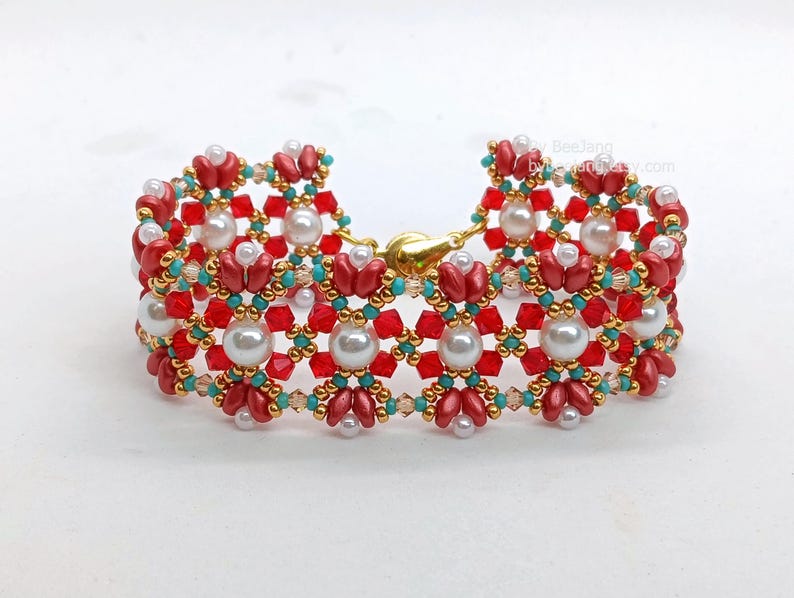 May include: A decorative bracelet with a floral pattern, made with red, white, gold, and turquoise beads. The bracelet has a gold clasp. The beads are small and round, with larger pearl-like beads.