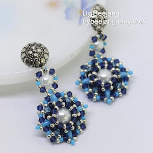 Puede incluir: Un par de pendientes colgantes con una cuenta de metal de tono plateado y un diseño de flor de cuentas azules y blancas. Los pendientes presentan una perla en el centro de cada flor.