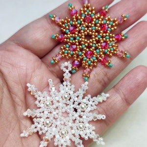 May include: Two beaded snowflake ornaments, one red and gold with clear crystals, and one white with clear crystals.