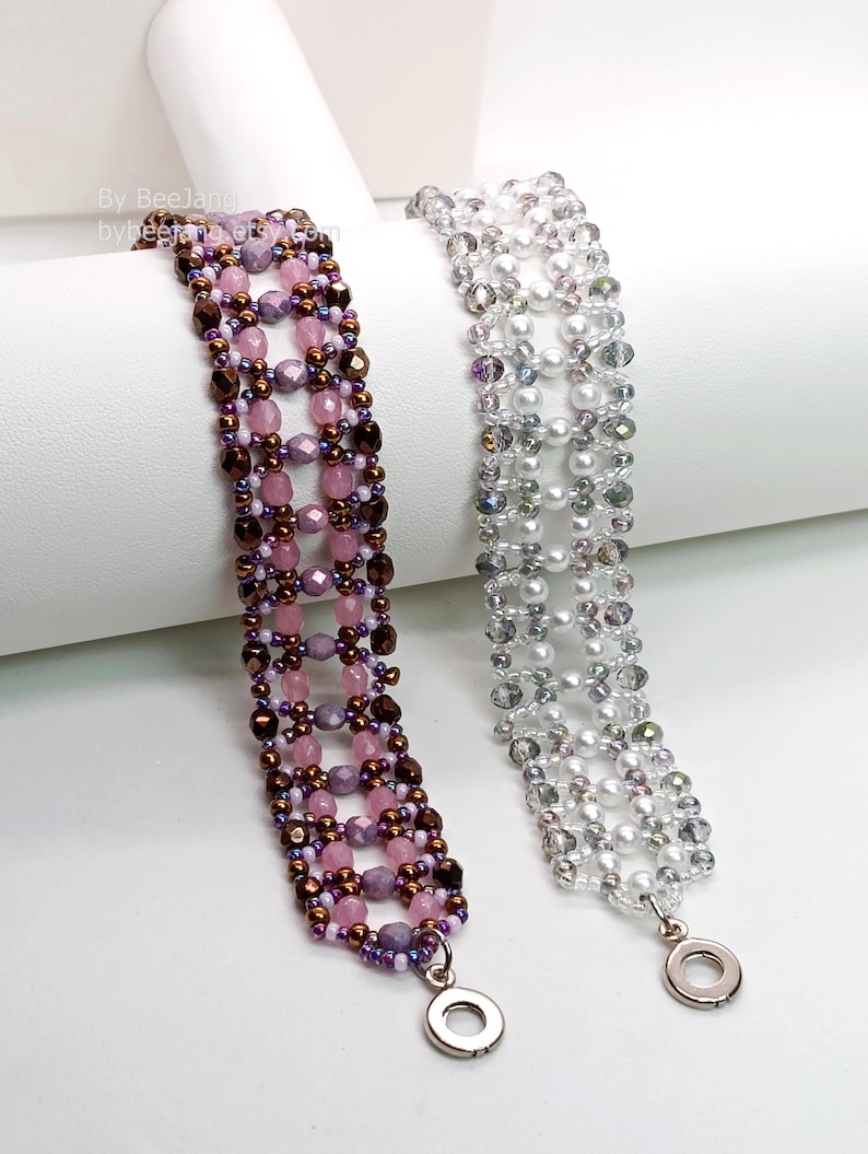 Two wide, handcrafted beaded cuff bracelets are draped over a white stand, showcasing an intricate Right Angle Weave lattice design. Each piece is meticulously woven with faceted bicone crystals, smooth round pearls, and delicate seed beads, secured with a metallic toggle clasp.

    Left: Purple and lavender beads accented by dark metallic bronze rounds and a silver clasp.
    Right: Clear crystals with white pearls and a silver clasp.