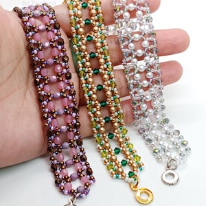 Three wide, handcrafted cuff bracelets are displayed, showcasing an intricate
Right Angle Weave lattice design. Each piece is meticulously woven with faceted bicone crystals, smooth round pearls, and delicate seed beads, secured with a metallic toggle clasp.
    Left: Purple and lavender crystals with copper beads.
    Center: Emerald and olive crystals with bronze pearls.
    Right: Clear crystals with white pearls and silver accents.