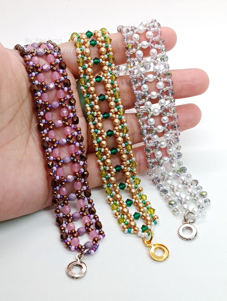 Three wide, handcrafted cuff bracelets are displayed, showcasing an intricate
Right Angle Weave lattice design. Each piece is meticulously woven with faceted bicone crystals, smooth round pearls, and delicate seed beads, secured with a metallic toggle clasp.
    Left: Purple and lavender crystals with copper beads.
    Center: Emerald and olive crystals with bronze pearls.
    Right: Clear crystals with white pearls and silver accents.