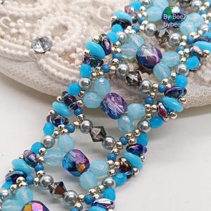 Puede incluir: Una pulsera de cuentas con una mezcla de cuentas azules, moradas y plateadas. La pulsera tiene un dise&ntilde;o en capas con varias formas y tama&ntilde;os de cuentas. El texto "by BeeJann" y "bybeejann.etsy.com" es visible.