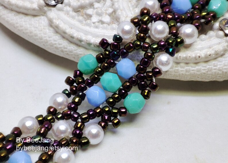 May include: A close-up of a beaded bracelet with a multi-strand design. The bracelet features brown iridescent beads, white pearls, and turquoise and light blue faceted beads. The bracelet is on a white surface.