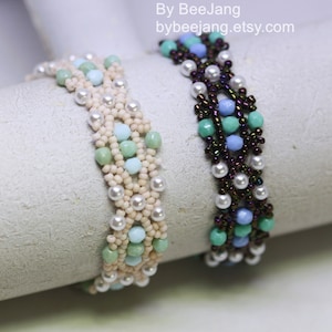 May include: Two beaded bracelets with a woven pattern. One bracelet is made with white, cream, and light blue beads. The other bracelet is made with dark brown, light blue, and green beads. The bracelets are displayed on a white surface. By BeeJang bybeejang.etsy.com