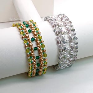 Two wide, handcrafted beaded cuff bracelets are draped over a white stand, showcasing an intricate Right Angle Weave lattice design. Each piece is woven with faceted bicone crystals, smooth round pearls, and seed beads, secured with a metallic toggle clasp.

    Left: Emerald and olive green crystals with gold-toned pearls and a gold clasp.
    Right: Clear crystals with white pearls and a silver clasp.