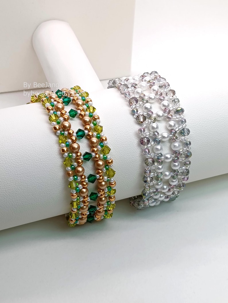 Two wide, handcrafted beaded cuff bracelets are draped over a white stand, showcasing an intricate Right Angle Weave lattice design. Each piece is woven with faceted bicone crystals, smooth round pearls, and seed beads, secured with a metallic toggle clasp.

    Left: Emerald and olive green crystals with gold-toned pearls and a gold clasp.
    Right: Clear crystals with white pearls and a silver clasp.