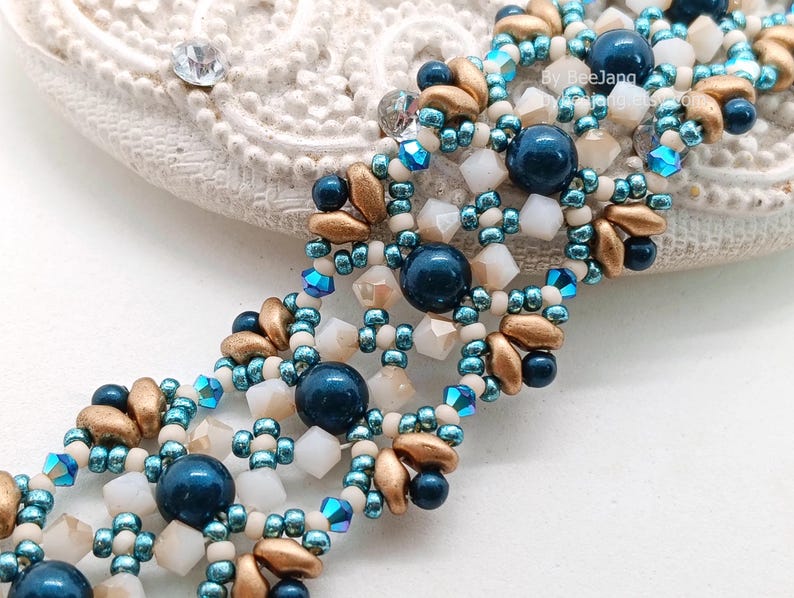 May include: A close-up of a beaded bracelet with navy blue, gold, and white beads. The bracelet has a multi-strand design with a mix of round and faceted beads. The beads are arranged in a repeating pattern, creating a textured and detailed look.