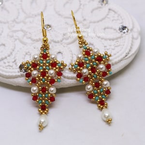 May include: A pair of gold dangle earrings with red, turquoise, and white beads. The earrings are shaped like a cross and have a pearl drop at the bottom.