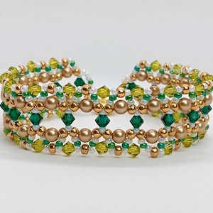 A wide, handcrafted "cuff" style beaded bracelet featuring an intricate lattice design. The piece is composed of emerald green and olive 4mm bicone crystals, metallic bronze round pearls, and delicate white and gold seed beads. The beads are intricately woven together using a right-angle weave stitch to form a series of interconnected diamond patterns.