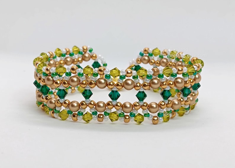 A wide, handcrafted "cuff" style beaded bracelet featuring an intricate lattice design. The piece is composed of emerald green and olive 4mm bicone crystals, metallic bronze round pearls, and delicate white and gold seed beads. The beads are intricately woven together using a right-angle weave stitch to form a series of interconnected diamond patterns.