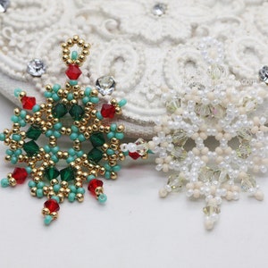 Two handcrafted, intricate beaded snowflake pendants or ornaments displayed on an ornate white surface. The left pendant features gold, turquoise, green, and red beads, while the right pendant features white, cream, and clear beads.