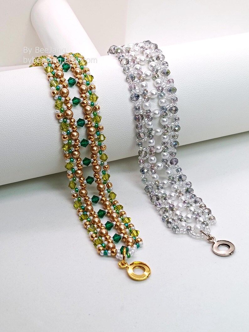 Two wide, handcrafted beaded cuff bracelets are draped over a white stand, showcasing an intricate Right Angle Weave lattice design. Each piece is woven with faceted bicone crystals, smooth round pearls, and seed beads, secured with a metallic toggle clasp.

    Left: Emerald and olive green crystals with gold-toned pearls and a gold clasp.
    Right: Clear crystals with white pearls and a silver clasp.
