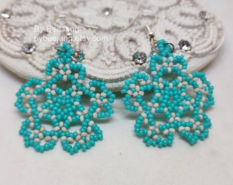 May include: A pair of turquoise and white beaded flower earrings. The earrings are made with small beads and feature a floral design. The earrings have silver-colored ear wires and are displayed on a white, lacy surface.