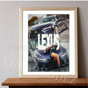 May include: Framed print featuring two dark blue Lexus cars. The word "LEXUS" is prominently displayed in white. A person is lying on the hood of the lower car. The print is displayed on a wooden surface.