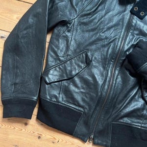 May include: Black leather jacket with a zipper closure, two front pockets, and a ribbed knit collar and cuffs. The jacket has a classic bomber style.