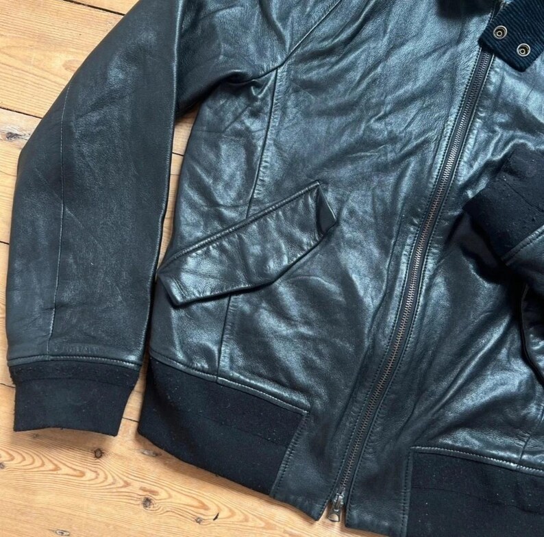 May include: Black leather jacket with a zipper closure, two front pockets, and a ribbed knit collar and cuffs. The jacket has a classic bomber style.