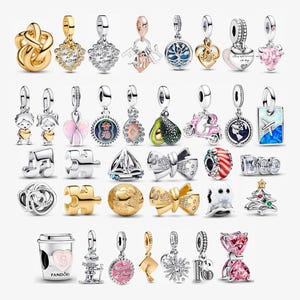 May include: A selection of silver and gold-coloured charm pendants with diverse designs, including hearts, bows, and travel themes. Some charms feature gemstones and detailed designs, suitable for bracelets or necklaces.
