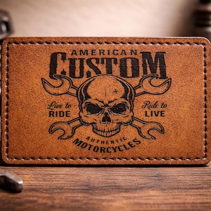 May include: A brown leather patch featuring the words "AMERICAN CUSTOM MOTORCYCLES" and a skull graphic with crossed wrenches. The patch also includes the phrases "Live to Ride" and "Ride to Live".