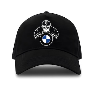 Può includere: Cappellino da baseball nero con grafica bianca di un motociclista con casco a scacchi e logo BMW. Il cappellino ha una visiera curva e una corona strutturata. Il design è centrato sulla parte anteriore.