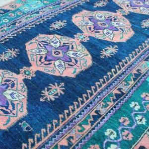 Puede incluir: Una alfombra rectangular con fondo azul marino y un patrón floral repetido en tonos melocotón, morado y verde azulado. La alfombra tiene un borde con diseños geométricos y un aspecto texturizado. La alfombra es adecuada para la decoración del hogar.