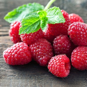 May include: A cluster of vibrant red raspberries with a textured, bumpy surface and a single sprig of bright green mint leaves resting on top, showcasing the natural details of the fruit and the fresh, serrated edges of the herb leaves.