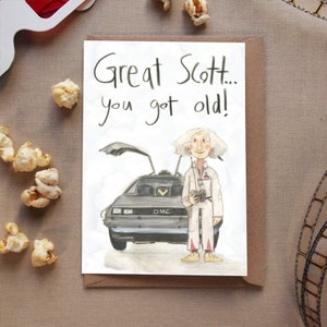 May include: A birthday card featuring a cartoon illustration of Doc Brown from the movie Back to the Future. The card has the text "Great Scott... you got old!" written on it.