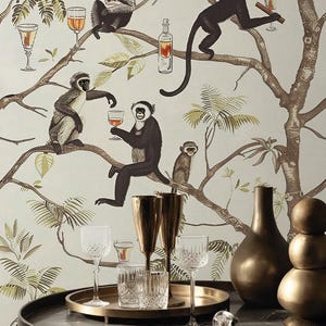 May include: Wallpaper featuring a pattern of monkeys in trees with glasses and bottles, set behind a round table with two gold-toned flutes, two crystal glasses, a gold tray, a dark vase, and a stacked gold sphere sculpture on a marble top.