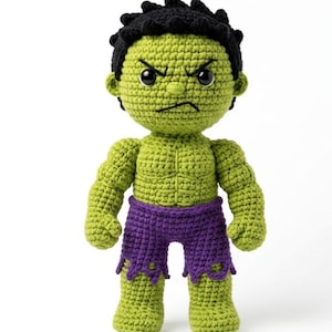 May include: A handmade crochet doll featuring a green skin tone, black hair, and purple shorts with a jagged hem. The figure has a muscular torso, defined facial features with black eyes, and a stern expression with a furrowed brow.