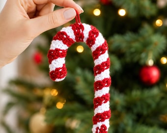 May include: A crochet candy cane ornament featuring a repeating spiral pattern of alternating red and white yarn. The J-shaped decoration includes a small matching red yarn loop at the top for hanging, showcasing a textured, handmade fibre construction.