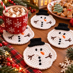 May include: A set of four round, white crocheted coasters shaped like snowmen, each featuring a black crocheted top hat, a small orange carrot nose, black button eyes, and brown stitched twig arms, arranged on a wooden surface.